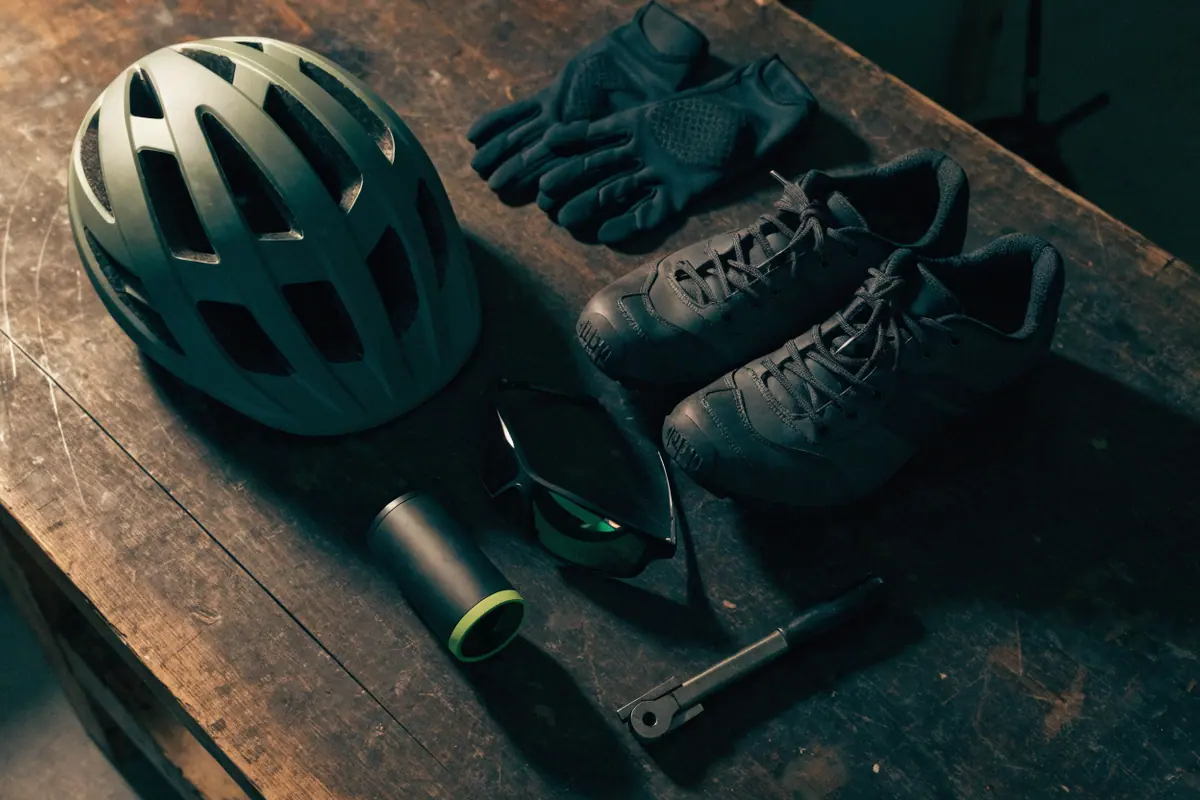 Capacete, luvas, sapatilha, óculos, farol e mini bomba de ciclismo sobre uma bancada de madeira